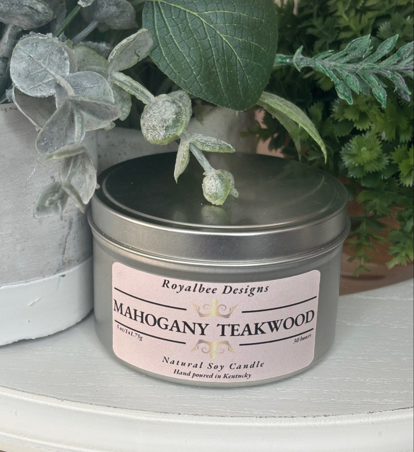 Mahogany Teakwood candle in a tin with a pink label sold by Royalbee Designs